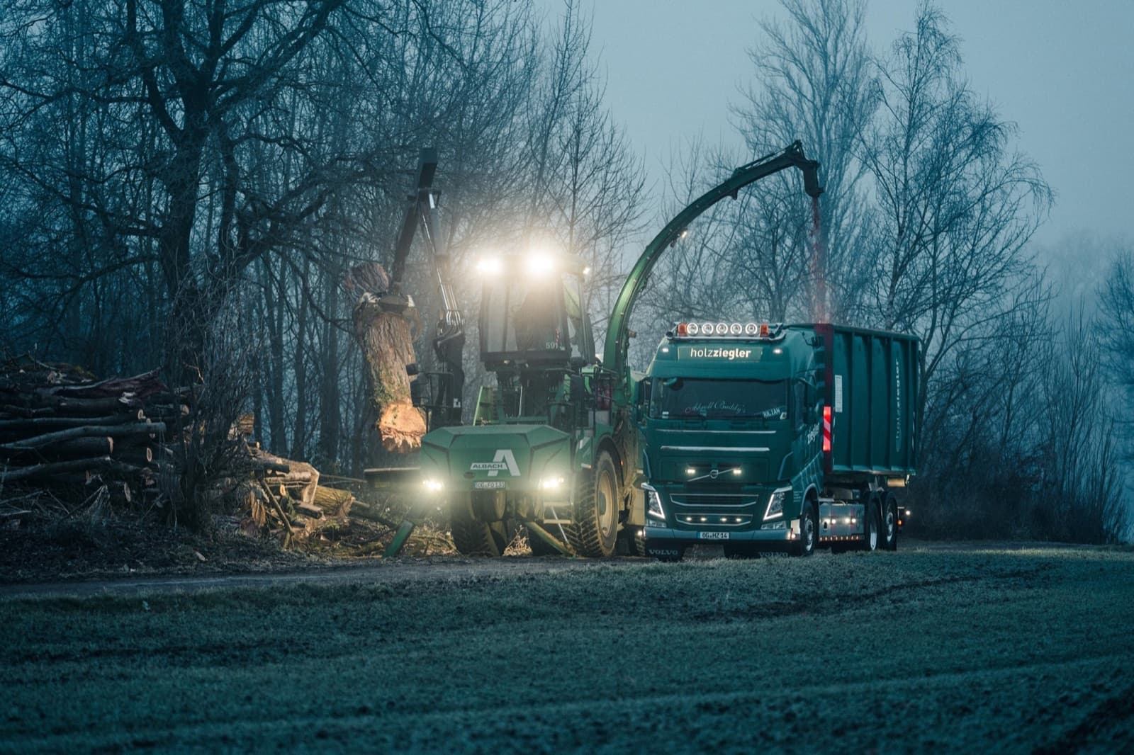 Abrollcontainerfahrzeug und mobiler Hacker im Morgengrauen am Waldrand