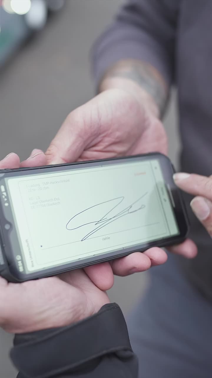 Fahrer hält ein Smartphone mit dem digitalen Abholbeleg vor einem Abrollcontainer